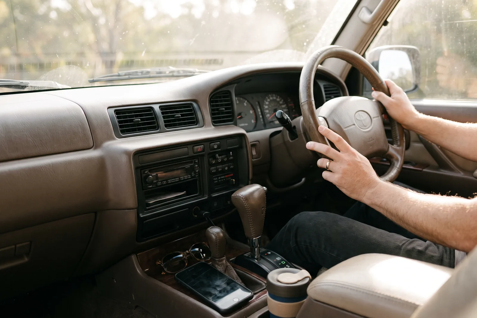 A phone lying face down on a car centre console with the dashboard visible in soft daylight