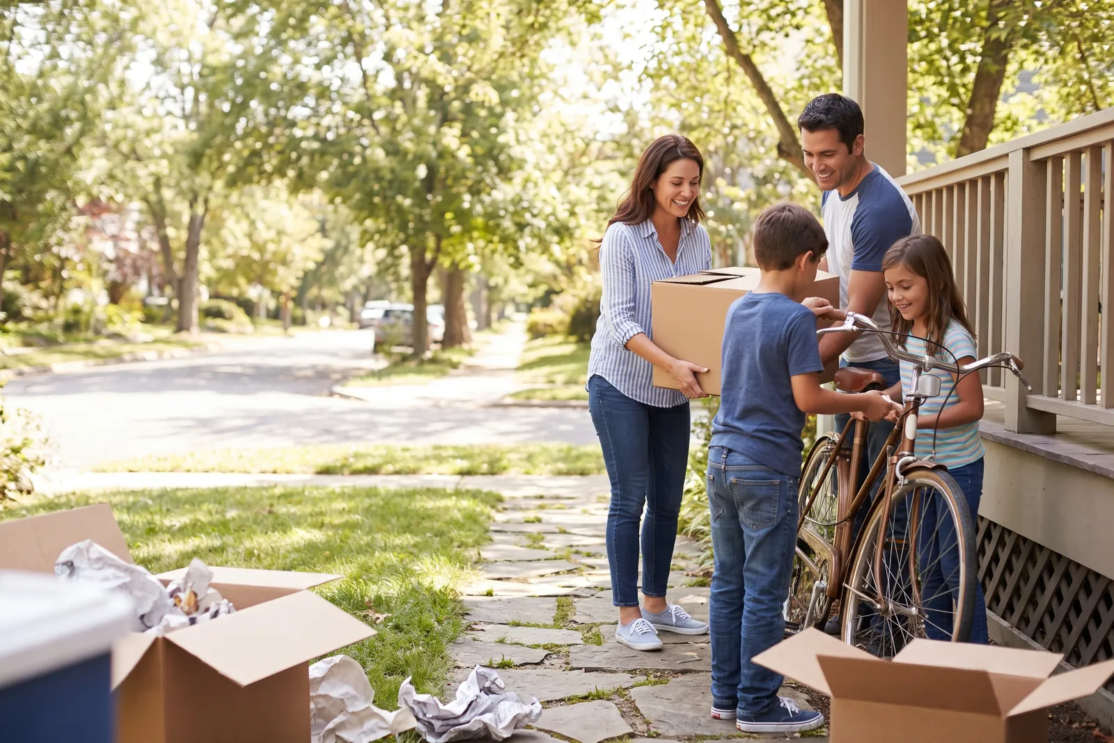 A family unloading cardboard moving boxes onto the front porch of a new house