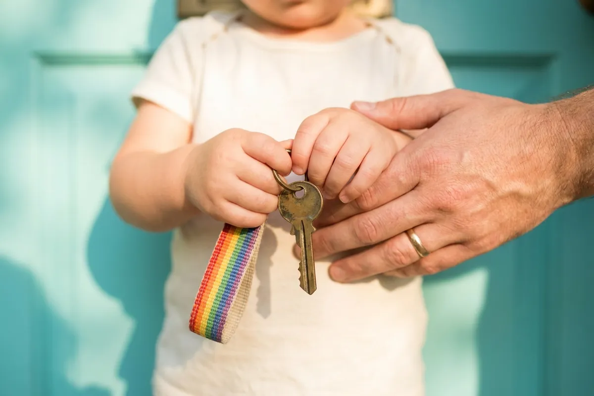 A child's hands holding a house key with a colorful keychain at the front door