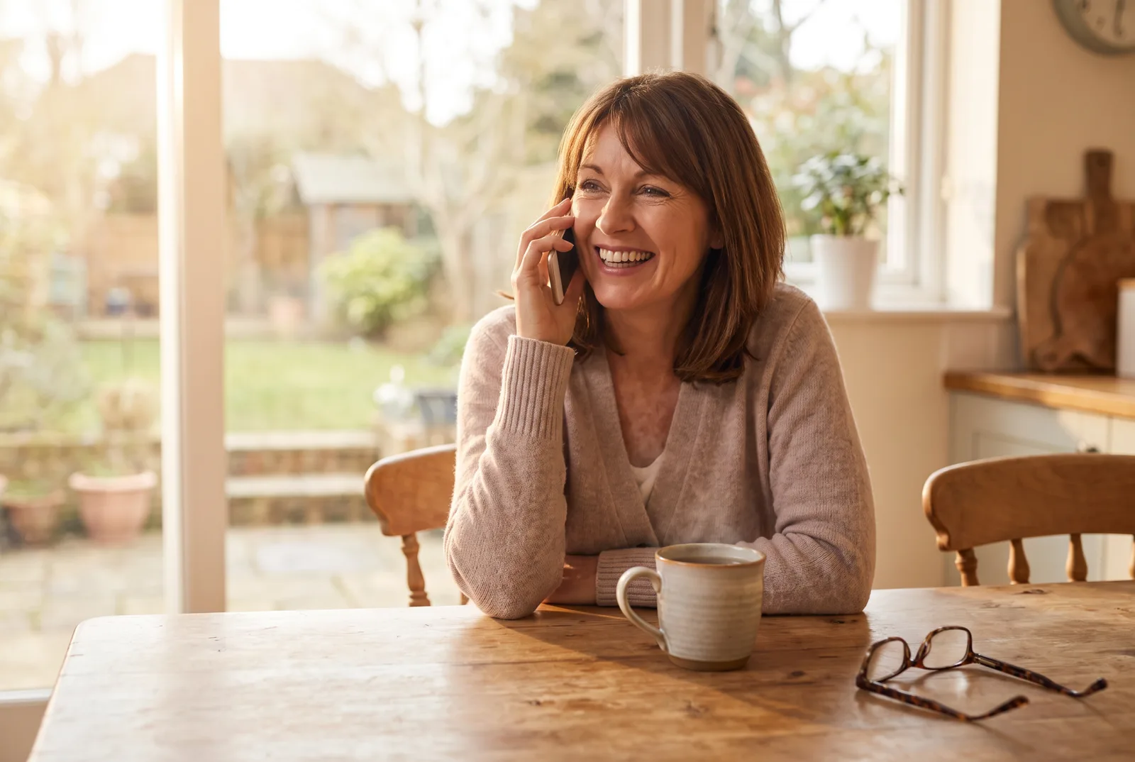 An older person holding a phone to their ear with a cup of tea on the table