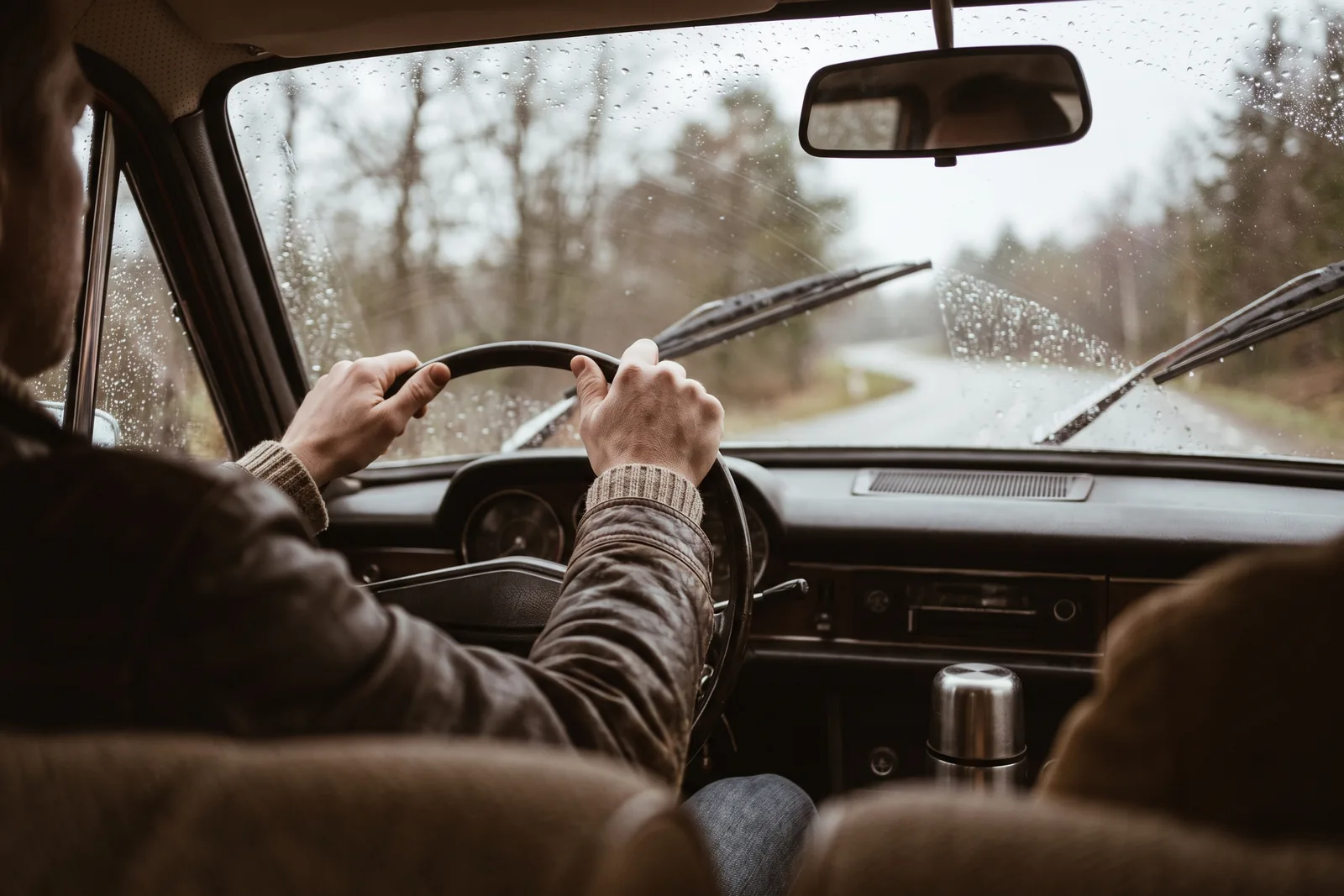 View through a rain covered windshield with wipers on and headlights reflecting off wet road