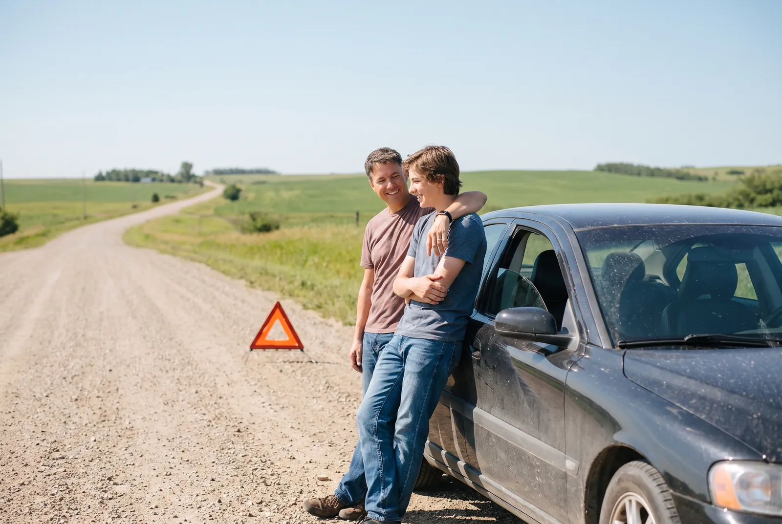 A red warning triangle placed on the road behind a stopped car on a quiet roadside at dusk